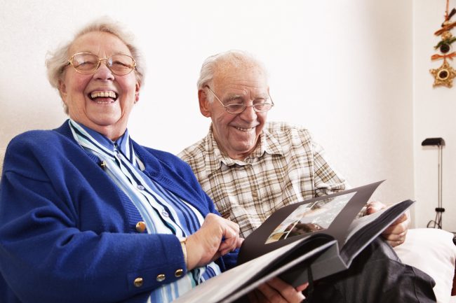 An elderly couple looking at a photo album and laughing.